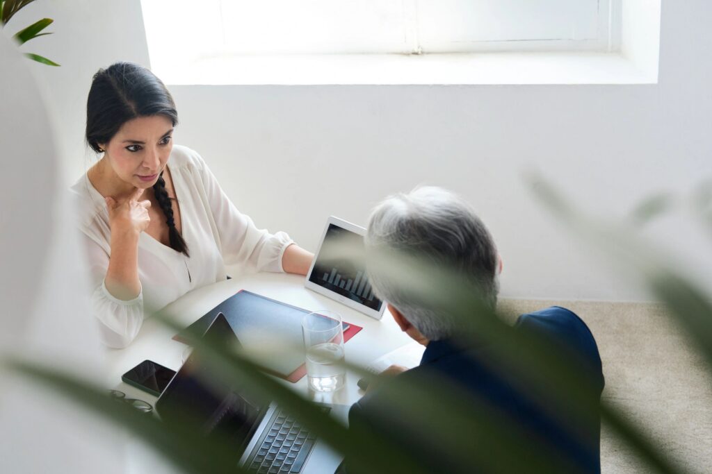 View from above of a Japanese senior businessman and beautiful CEO businesswoman sitting on a meeting table talking about growth graphics and new projects ideas for investment in a workplace.