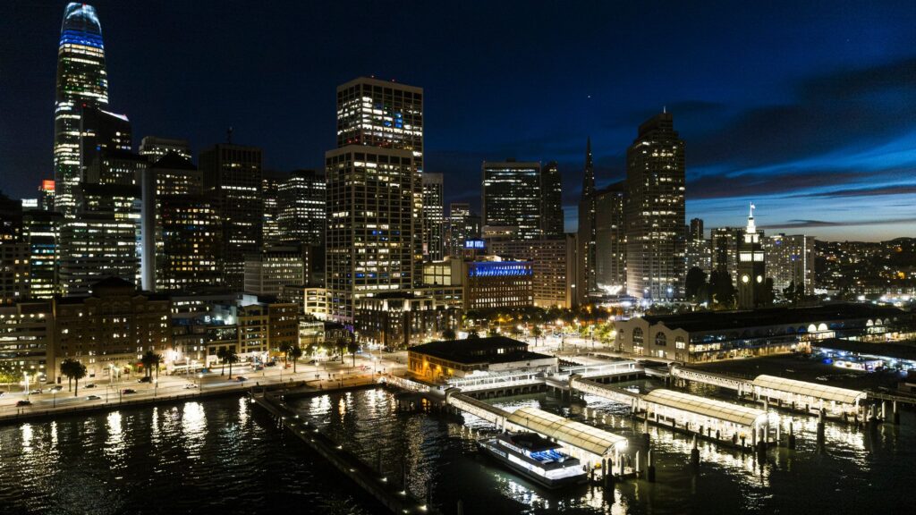 Waterfront terminals glow beneath towering skyscrapers. Blue hour view of South Beach district in San Francisco, California.